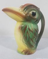 Front side view of the ceramic toucan bird pitcher showing detailed feather pattern and color glaze transitioning from green to yellow with brown highlights.