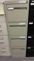 Front view of olive-gray 4-drawer filing cabinet showing all drawers with label holders.