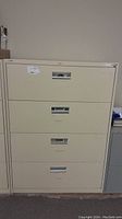 Front view of large beige 4-drawer metal filing cabinet, showing all drawer handles and overall condition.