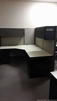 Full view of the L-shaped office cubicle showing the desk, panels, and overhead storage