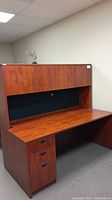 Side-angle view of cherry wood finished executive desk with three drawers on the left and upper hutch cupboards