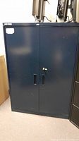 Full front view of the black steel storage cabinet with closed double doors and integrated handles.