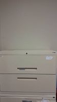 Front view of a beige short 2 drawer filing cabinet, closed drawers, lock visible on top drawer.