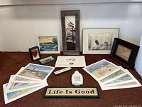Full lot layout showing art prints, framed pictures, decorative signs, and ornaments arranged on carpet against wall.
