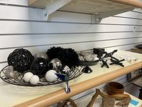 Full view of black wire tray with a variety of black, white, and metallic decorative balls and small decor items on shelf.