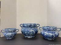 Front view of three blue and white Asian-themed ceramic bowls with bird motifs and scalloped edges, varying in size and each with two handles.