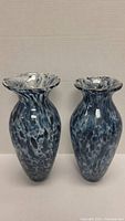 Pair of blue and white speckled glass vases standing side by side on a white surface with a plain background.