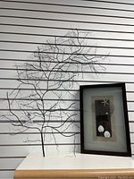 Metal branch wall hanging displayed on a white slatwall next to beach themed shadow box.