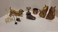 Full lot view showing brass horse head bookends, brass dog figurine, candle holder, mug, shoe figurine, incense holders and other small brass items arranged on a white background.