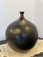 Front view of a large black ceramic pot with bulbous body and narrow neck on a cloth surface.