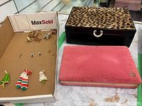 Photo showing pink velvet jewelry box, leopard print jewelry box, and cardboard tray with costume Christmas pins and earrings