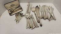 Flatware including multiple butter knives, appetizer forks, a serving fork and knife, and additional cutlery pieces.