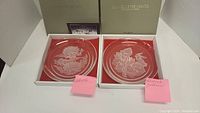 Two Hoya Crystal plates in original boxes, each with a different flower etching labeled with pink sticky notes reading "Freesia" and "Magnolia"