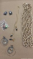Full lot of mixed jewelry items including necklaces, earrings, and loose stones on brown background