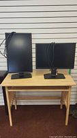Two Dell 24-inch monitors on a wooden folding desk with keyboard tray, one monitor vertical and one horizontal, cables attached.