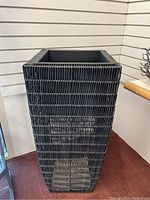 Side view showing tall plant stand with black wicker style texture.