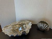 Two silver colored shell decor pieces on black surface, larger shell bowl on left and smaller shell on right.