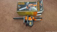 Photo showing Black & Decker chainsaw with original packaging box behind it on carpeted floor.