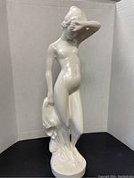 Front view showing the standing white ceramic nude woman figurine with arm covering her face and draped cloth.