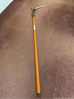 Full view of the closed telescoping branch cutter showing its extended orange handle and curved blade.