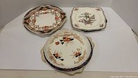 Photo showing three vintage plates with floral and geometric patterns laid side by side on white background.