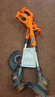 Two Black & Decker battery-powered weed trimmers paired with a Black & Decker manual. Both trimmers have orange handles and black trimming heads with some wear visible on one of the units.