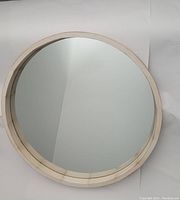 Top-down view of round mirror showing clear reflective glass and white washed wooden frame with visible wood grain details.