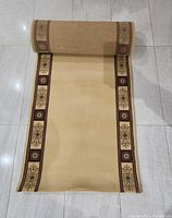 Photo of the carpet runner partially rolled out showing the floral and geometric border design and light brown base.