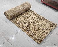 Carpet runner rolled partially open showing sand-beige color with floral patterns and border design.