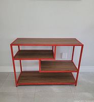 Front view of the console table showing the red metal frame, wood shelves, and asymmetric shelf arrangement.