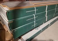 Several stacked boxes of engineered hardwood flooring, green and white packaging labeled with care instructions and storage guidance.