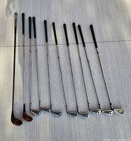 Full set of Wilson golf irons, drivers, and additional Ping driver laid on a white surface