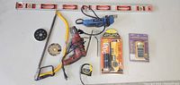 Wide view of all tools spread out, showing level, saw, drill, rotary tool, tape measure, and boxed measuring devices.