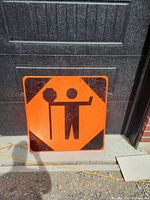 Front view of large orange construction sign depicting a traffic controller figure holding a stop paddle and a pole