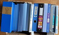Top view of all 14 binders arranged side by side showing the variety of widths and colors, mostly blue.