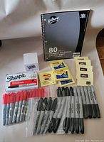 Photo showing Hilroy spiral notebook, Sharpie markers in red and black, Post-it notes, and Offix labels arranged on a surface.