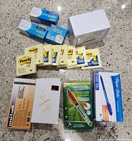 Photo of multiple new office supply items on a granite countertop. Items include 10 yellow Post-it Note pads, two rolls of Scotch Magic Tape, a box of Paper Mate pens, a boxed Uni-Ball pen, and a Ticonderoga permanent marker package.