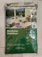 Photo showing the Modular Outdoor Protective Cover in original packaging with branding, images of the cover on outdoor furniture, and product details.