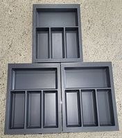 Three anthracite matt plastic cutlery trays with multiple compartments arranged on concrete floor