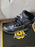 Side view of one black SWAT boot on top of the box showing leather upper, laces, padded ankle and treaded sole.