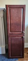Front exterior view of the pantry cabinet showing two dark wood paneled doors with round knobs.
