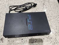 Black PS2 Slim console with power cord visible, placed on a granite countertop, photo taken from above.