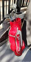 Full view of red and white Spalding golf bag containing multiple left-handed golf clubs.