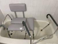 Shower seat with padded legs and backrest inside bathtub, showing adjustable legs with suction cup feet and padded seat area.