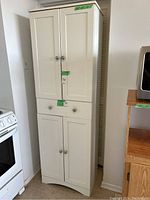 Front view of the white laminate kitchen cabinet showing upper storage doors, middle drawer, and lower storage doors with some wear visible at base.