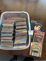 Bin containing two tall stacks of assorted music CDs in jewel cases and the Elvis American Idol book propped nearby.