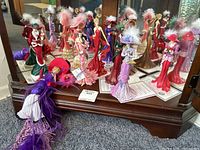 Ten collectible figurines displayed on wooden surface in front of a mirror, showing detailed costumes and hats with feathers and certificates of authenticity.