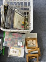Crate containing multiple plastic cases with cross stitch threads and kits, and three small gold frames.