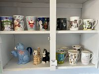 View of all items including cat-shaped tea pot, salt and pepper shakers, and cups arranged on shelf