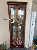 Front view of wood corner curio cabinet with glass door, mirrored back, and some figurines inside (not included).